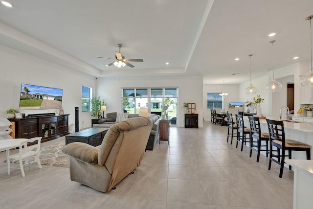 living room featuring light tile floors, sink, a raised ceiling, and ceiling fan with notable chandelier