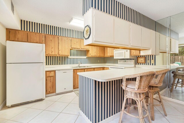 kitchen featuring a kitchen breakfast bar, a textured ceiling, white appliances, kitchen peninsula, and light tile flooring