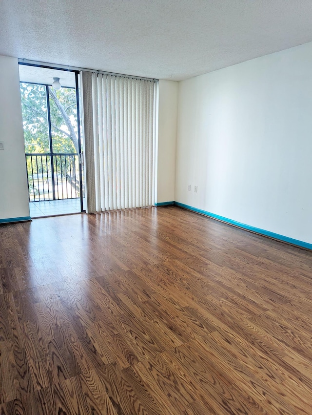 spare room featuring a wall of windows, wood-type flooring, and a textured ceiling