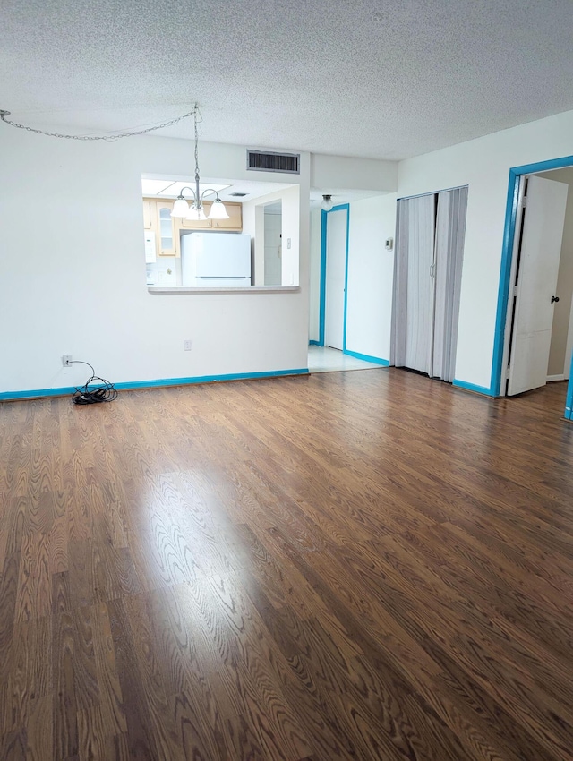 unfurnished living room with dark hardwood / wood-style floors, a notable chandelier, and a textured ceiling