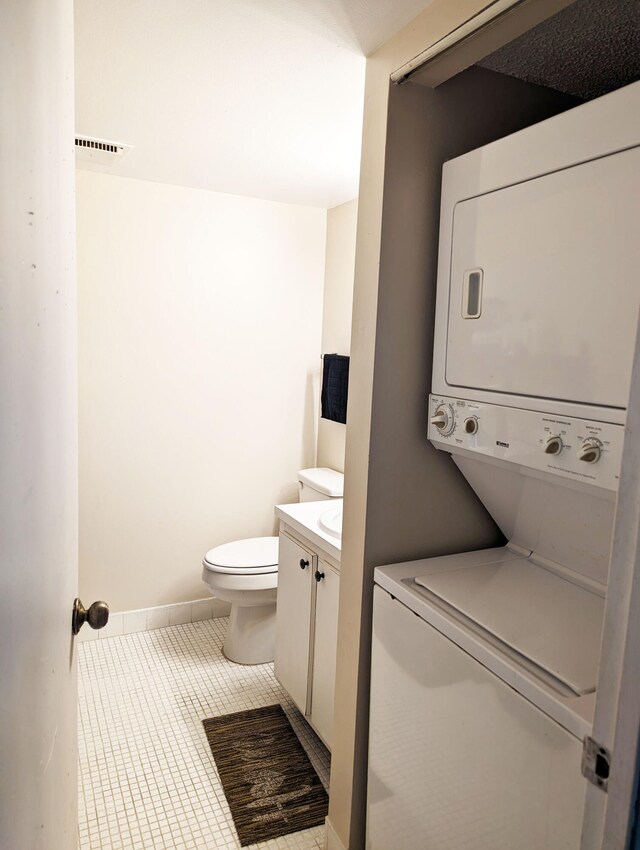 bathroom featuring vanity, toilet, stacked washer / dryer, and tile patterned flooring