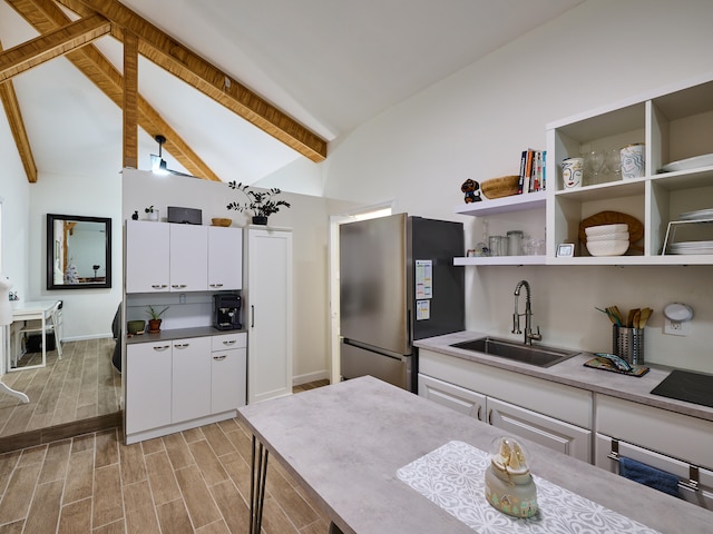 kitchen with lofted ceiling with beams, stainless steel fridge, black electric cooktop, white cabinetry, and sink