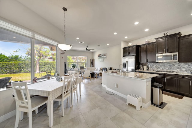 kitchen featuring dark brown cabinetry, appliances with stainless steel finishes, light stone countertops, backsplash, and hanging light fixtures