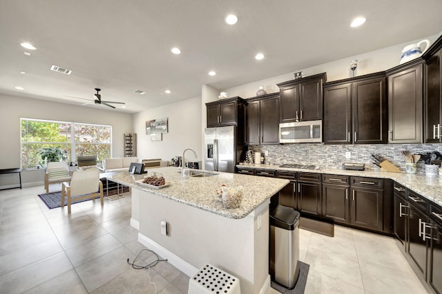 kitchen with light stone counters, a center island with sink, stainless steel appliances, sink, and ceiling fan