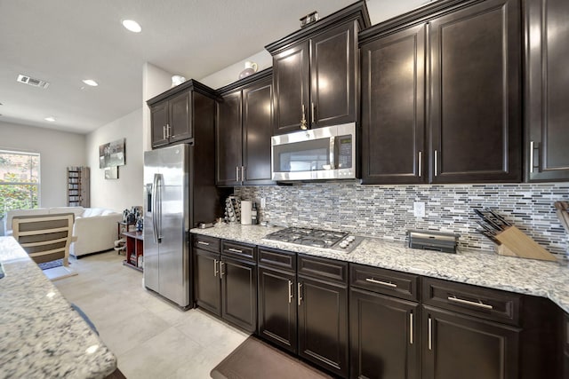 kitchen featuring stainless steel appliances, light stone counters, dark brown cabinetry, and decorative backsplash