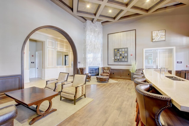 living area with beam ceiling, coffered ceiling, sink, light hardwood / wood-style floors, and a high ceiling