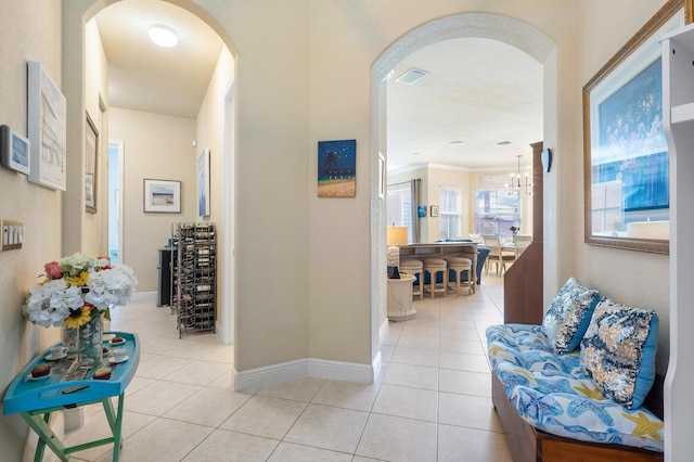 hall with light tile patterned flooring, ornamental molding, and a notable chandelier