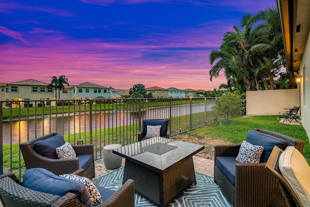 patio terrace at dusk with outdoor lounge area, a water view, and a lawn