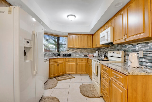 kitchen featuring light tile flooring, backsplash, a tray ceiling, light stone countertops, and white appliances