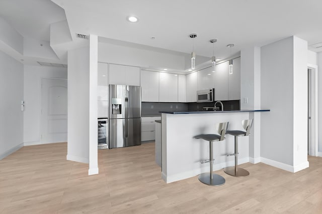 kitchen with white cabinets, a breakfast bar area, decorative light fixtures, kitchen peninsula, and stainless steel appliances