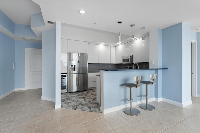 kitchen featuring pendant lighting, white cabinets, a breakfast bar area, kitchen peninsula, and stainless steel appliances