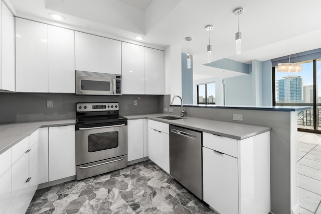 kitchen featuring kitchen peninsula, stainless steel appliances, sink, pendant lighting, and white cabinets