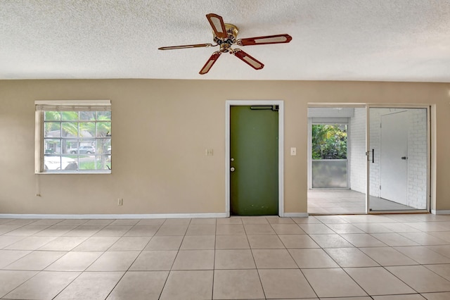 unfurnished room with ceiling fan, a healthy amount of sunlight, light tile patterned floors, and a textured ceiling