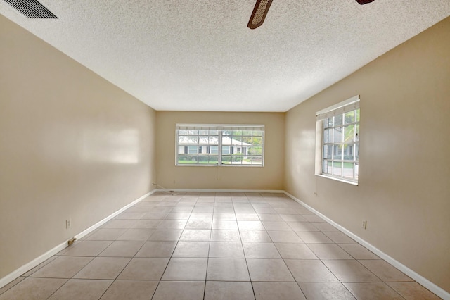 tiled empty room with a wealth of natural light, ceiling fan, and a textured ceiling