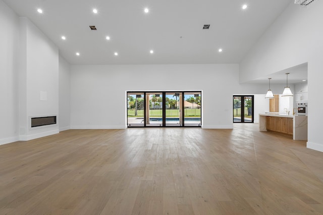 unfurnished living room featuring sink, light hardwood / wood-style floors, high vaulted ceiling, and french doors