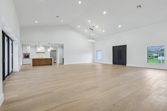 unfurnished living room featuring high vaulted ceiling, sink, and light wood-type flooring