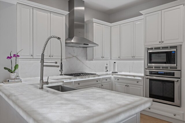 kitchen with wall chimney exhaust hood, tasteful backsplash, white cabinetry, and appliances with stainless steel finishes