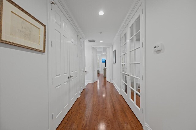 corridor with dark wood-type flooring, ornamental molding, and french doors