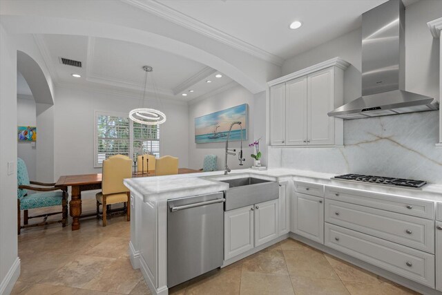 kitchen featuring a tray ceiling, kitchen peninsula, stainless steel appliances, decorative light fixtures, and wall chimney exhaust hood