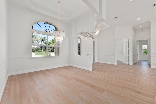 empty room with crown molding, a high ceiling, a notable chandelier, and light hardwood / wood-style floors