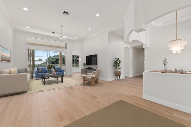 living room featuring ceiling fan with notable chandelier, ornamental molding, and light hardwood / wood-style flooring