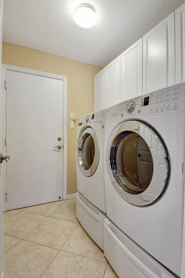 washroom featuring washer and dryer, cabinets, a textured ceiling, and light tile flooring