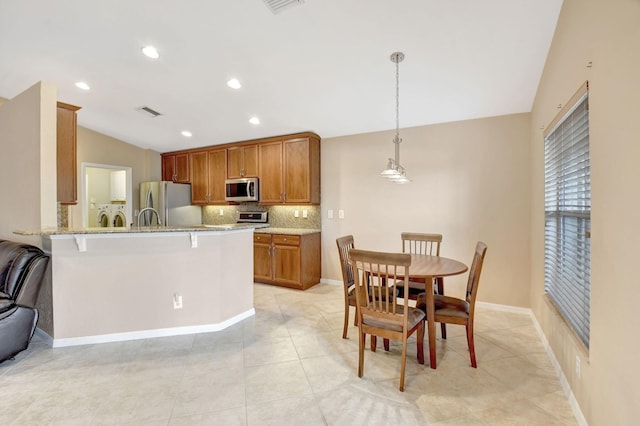 kitchen featuring tasteful backsplash, stainless steel appliances, light tile flooring, decorative light fixtures, and light stone counters