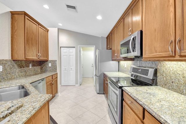 kitchen with lofted ceiling, stainless steel appliances, light stone counters, backsplash, and light tile floors