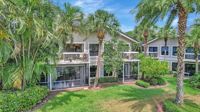 rear view of property featuring a sunroom, a yard, a balcony, and stucco siding