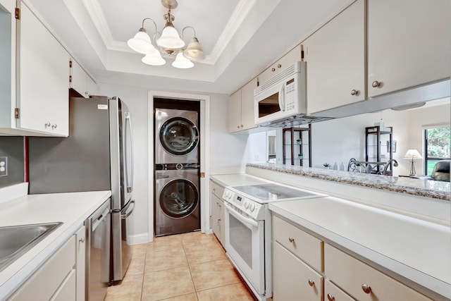 kitchen featuring white appliances, stacked washer / dryer, white cabinets, light countertops, and a tray ceiling