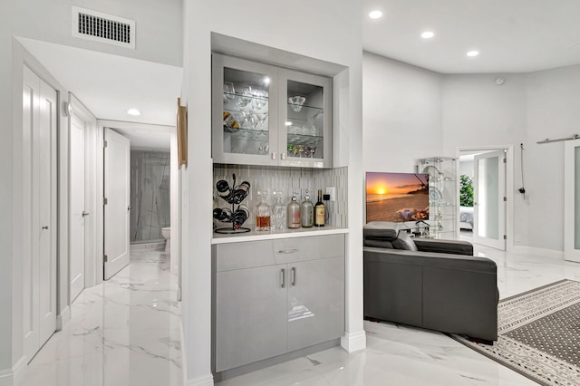 bar featuring a high ceiling, gray cabinetry, light tile floors, and backsplash