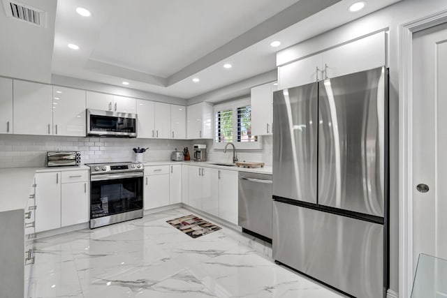 kitchen featuring light tile flooring, stainless steel appliances, backsplash, a raised ceiling, and white cabinetry