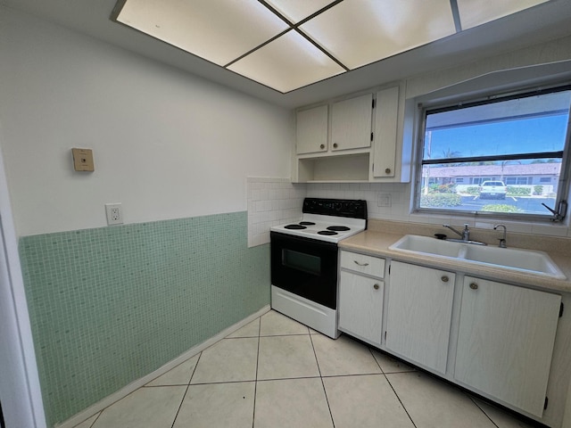 kitchen with light tile flooring, tasteful backsplash, white electric range oven, white cabinets, and sink