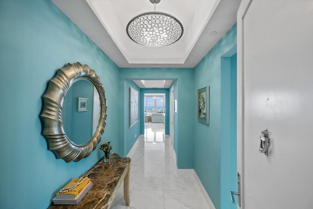 corridor featuring a tray ceiling, baseboards, and marble finish floor