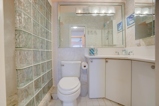 bathroom with a tile shower, tile patterned floors, toilet, vanity, and tile walls