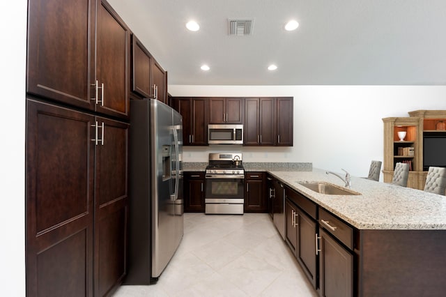 kitchen featuring light stone countertops, dark brown cabinetry, stainless steel appliances, and sink