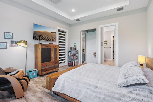 bedroom featuring light hardwood / wood-style floors, ensuite bathroom, and a raised ceiling