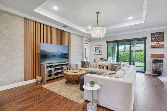 living room with an inviting chandelier, a tray ceiling, and ornamental molding