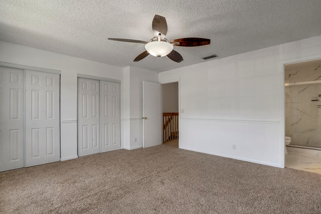 unfurnished bedroom with ceiling fan, carpet flooring, a textured ceiling, connected bathroom, and multiple closets