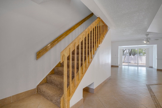 stairway featuring tile flooring, ceiling fan, and a textured ceiling