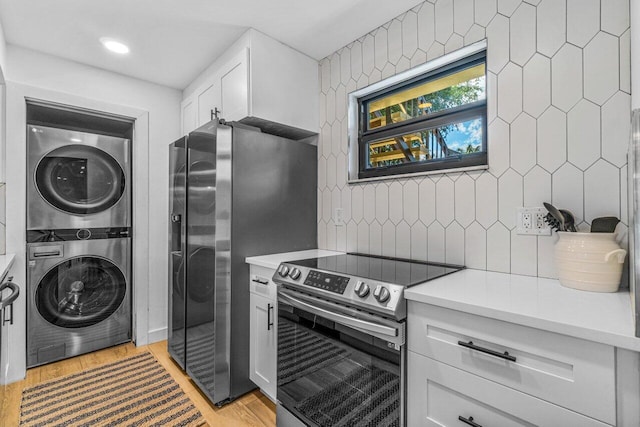 kitchen with decorative backsplash, light wood-type flooring, appliances with stainless steel finishes, stacked washer / drying machine, and white cabinetry