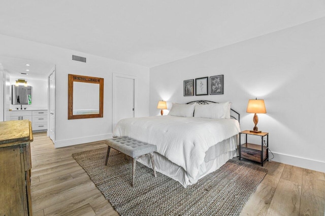 bedroom with light hardwood / wood-style flooring, ensuite bath, and sink