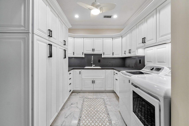 laundry room featuring ceiling fan, sink, cabinets, washing machine and dryer, and crown molding