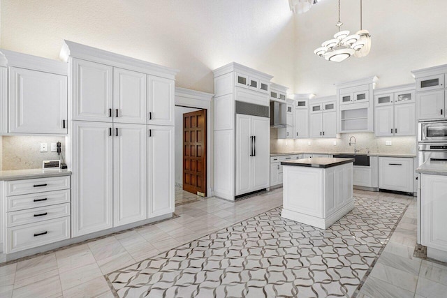 kitchen with built in appliances, decorative backsplash, white cabinetry, and decorative light fixtures