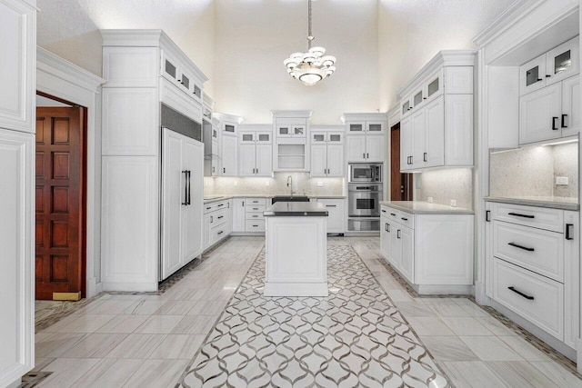 kitchen with white cabinets, built in appliances, decorative light fixtures, and backsplash