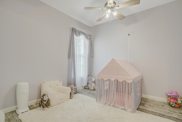 bedroom featuring a nursery area, light hardwood / wood-style flooring, and ceiling fan