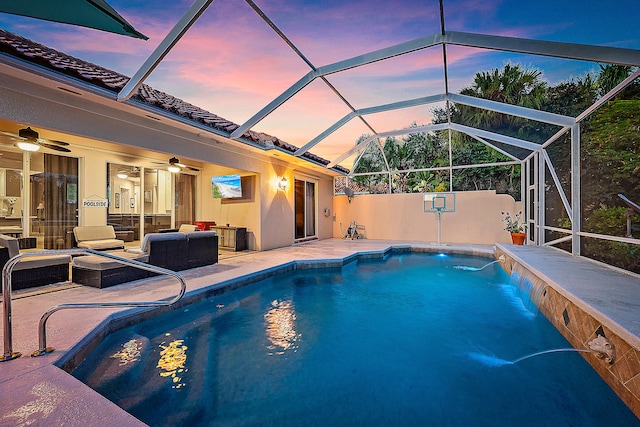 pool at dusk featuring a patio, pool water feature, glass enclosure, ceiling fan, and an outdoor hangout area