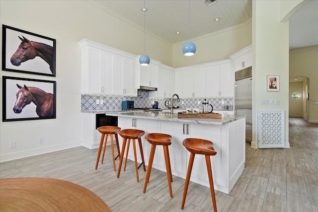 kitchen featuring white cabinets, light stone countertops, a high ceiling, and tasteful backsplash