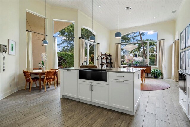 kitchen with light hardwood / wood-style floors, crown molding, an island with sink, white cabinets, and decorative light fixtures