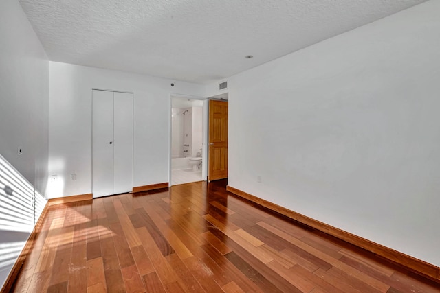 unfurnished bedroom with wood-type flooring, ensuite bath, and a textured ceiling